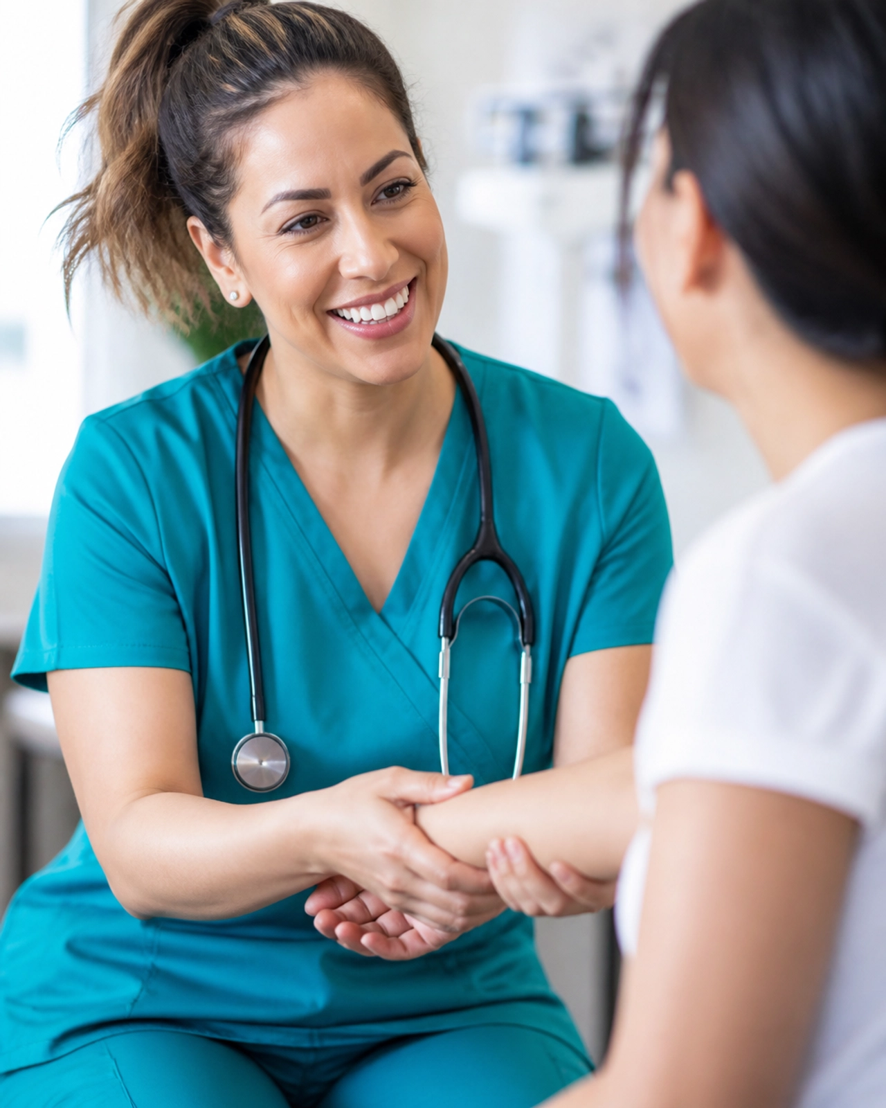 A healthcare provider in teal scrubs examining a patient's arm in a bright, clean clinical room.